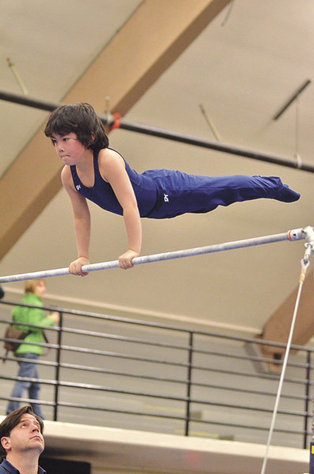 Coach Bryan Garoutte looks on as Leo Uyekawa swings through his high bar routine.