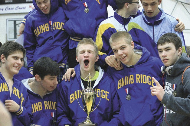 Members of the Bainbridge High School wrestling team gather around their Metro League trophy after the team’s big win at the conference meet at Nathan Hale High. The Spartan wrestlers will head to the state meet in the Tacoma Dome for the 25th edition of the Mat Classic.