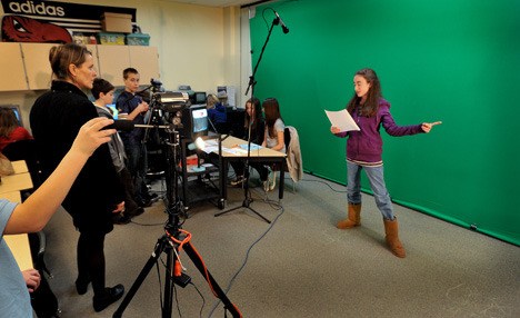 Sakai teacher Terri Atkinson watches as weather reporter Leah Potter works the green screen during the weather segment. The students produce a live daily news