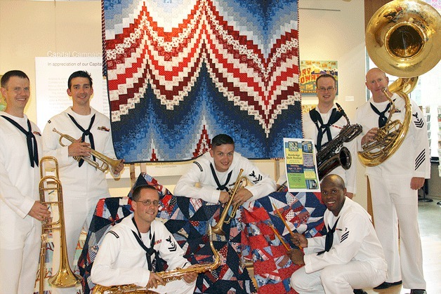 Members of the Northwest Navy Band “Deception Brass” gather around a quilt from the Bainbridge Island Modern Quilt Guild during Military Appreciation Day at BIMA.