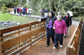 Kathy Anderson helps her mom Sue Yonemitsu across the cedar plank bridge at the site.