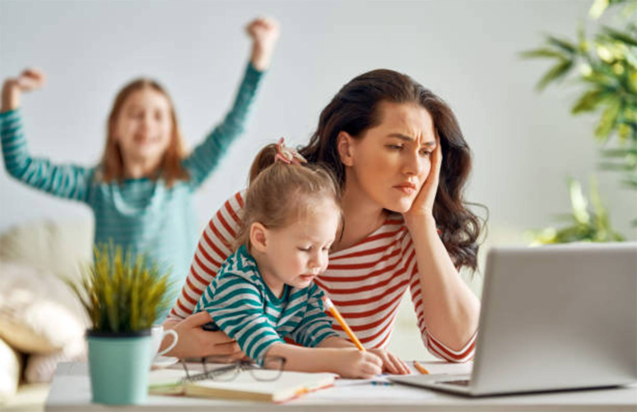 A frustrated mom helps kids at computer with online learning. Getty Images stock photo