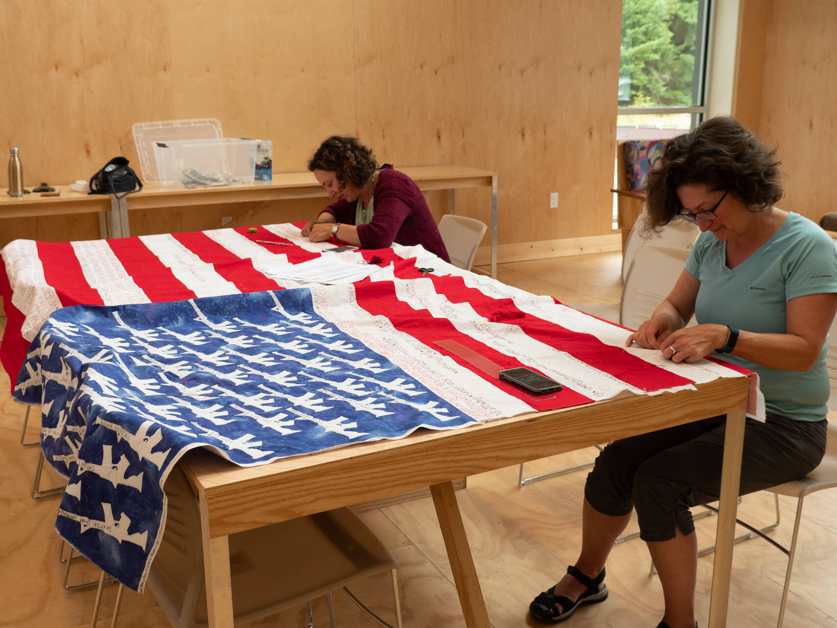 Deborah Ruddnick, right, and Naomi Spinak, left, embroider more than 100 names onto the white stripes of the flag quilt dedicated to victims of mass shootings in the United States. Courtesy photo