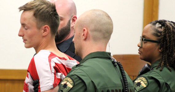 Elisha Meyer/Kitsap News Group
23-year-old double homicide suspect Seth South is restrained by shackles and a trio of correction officers in court Oct. 10. Officers began to accompany him before the judge after he made a sudden move toward the gallery of the courtroom.